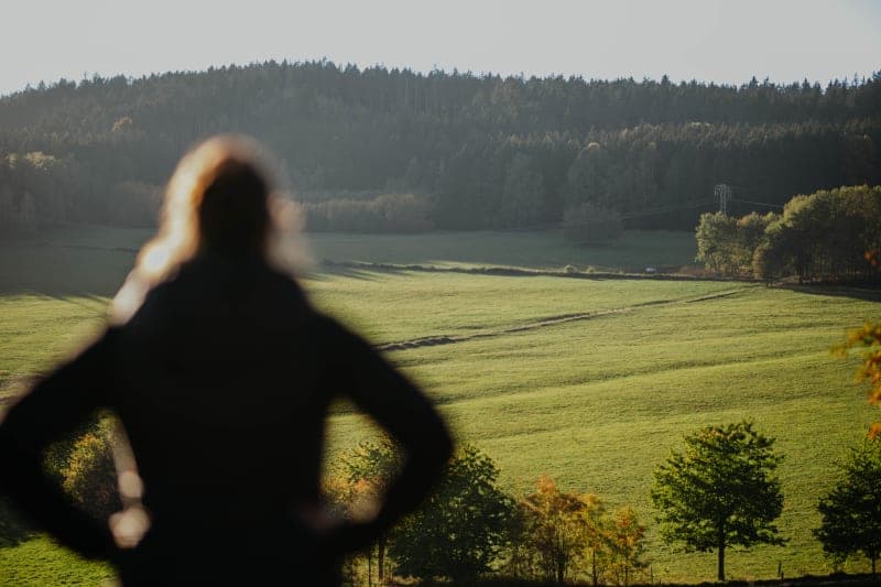 Silhouette einer Person mit Blick über grüne Wiesen und bewaldete Hügel der Rhön im Abendlicht