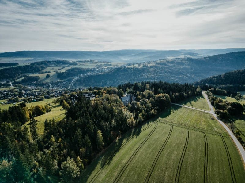 Luftaufnahme des Hotels Hoher Hahn umgeben von grĂĽnen Wiesen und ThĂĽringer Waldlandschaft mit HĂĽgeln im Hintergrund