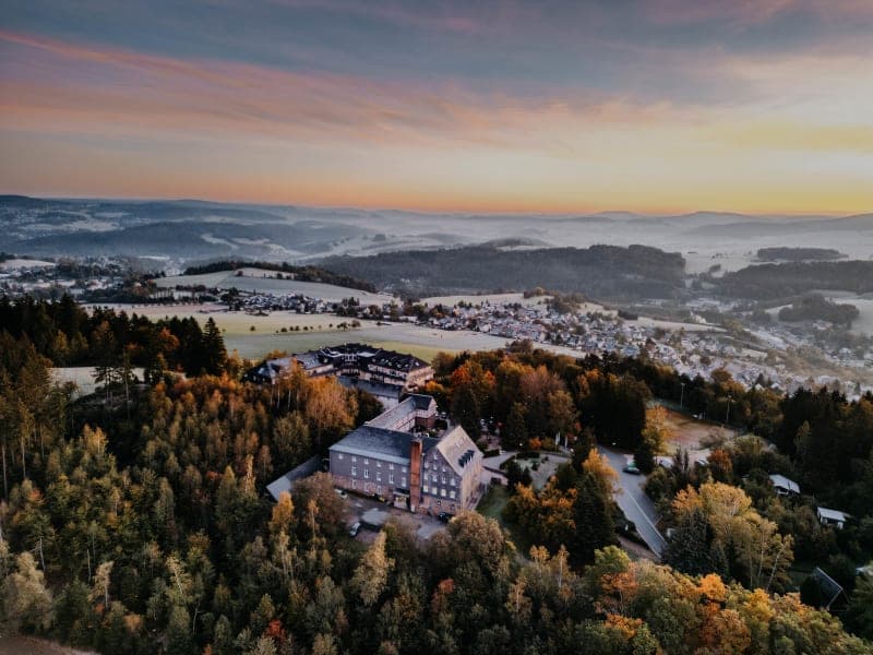 Luftaufnahme des Hotels Hoher Hahn umgeben von Herbstwald bei Sonnenuntergang im Erzgebirge