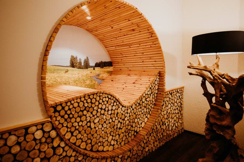 Runde Holznische mit gestapelten Holzscheiben und Blick auf Naturlandschaft im Wellnessbereich